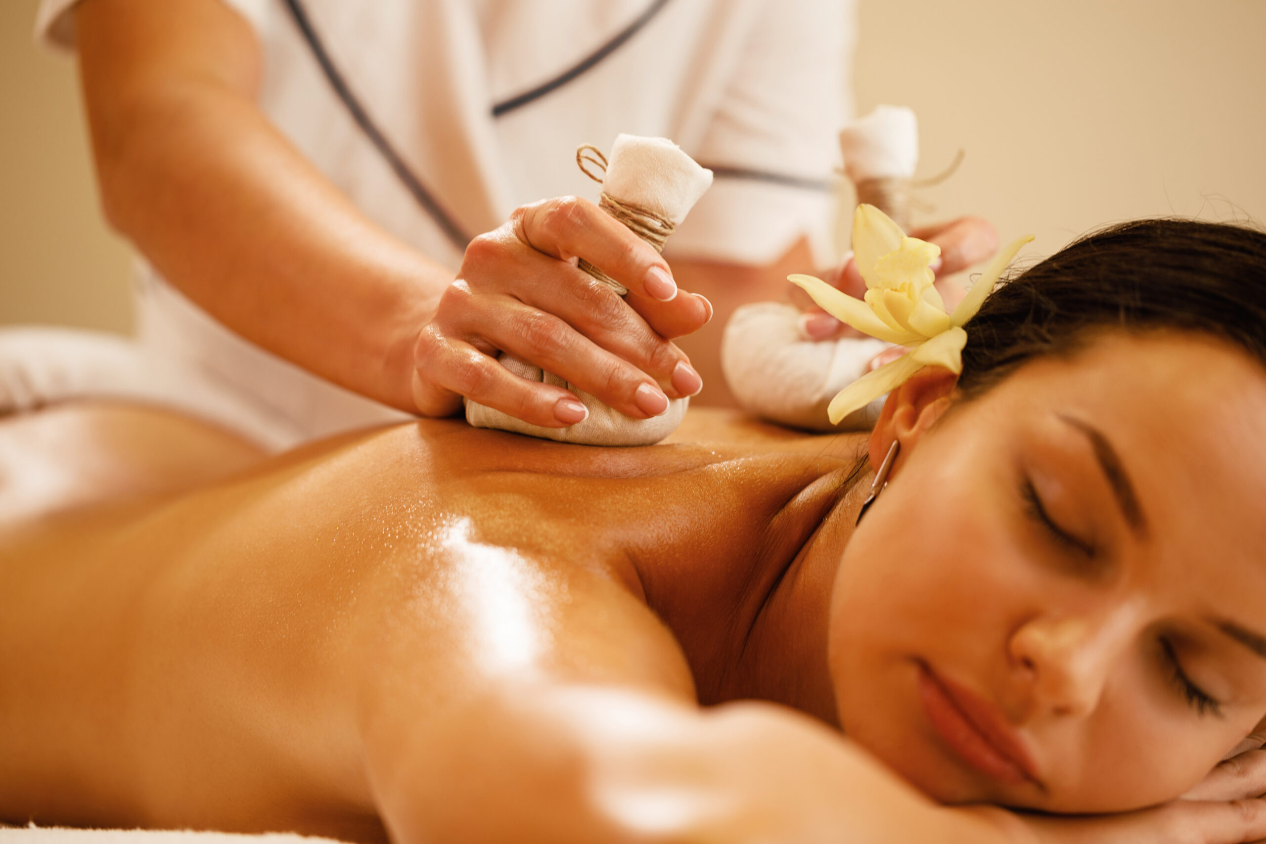 Close-up of relaxed woman getting back massage with herbal balls at health spa.